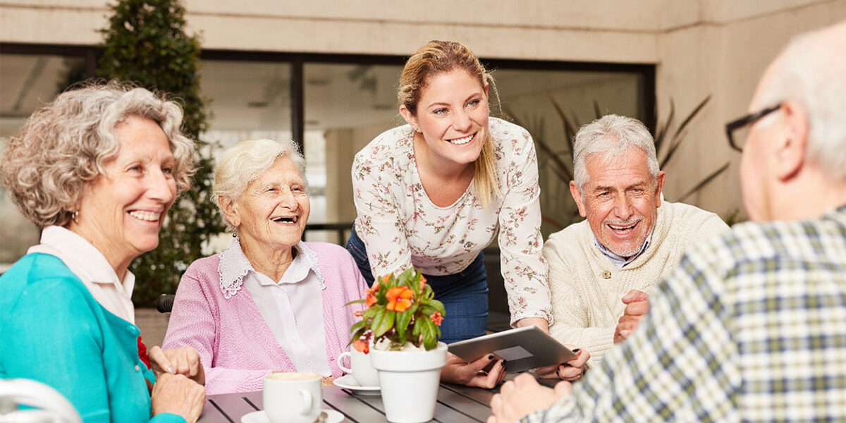 bellevue-senior-living-55-plus-living-vs-independent-living-fb Bellevue | Group of happy senior citizens and staff member sitting at table