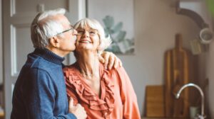 Senior couple in their new Senior Living home Man is giving his wife a kiss on the cheek.